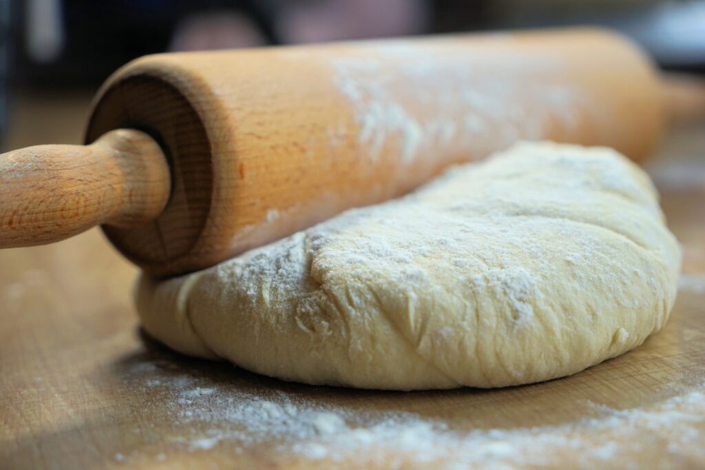 un matterello poggiato su un impasto da cuocere in forno. tutto poggia su un piano in legno infarinato